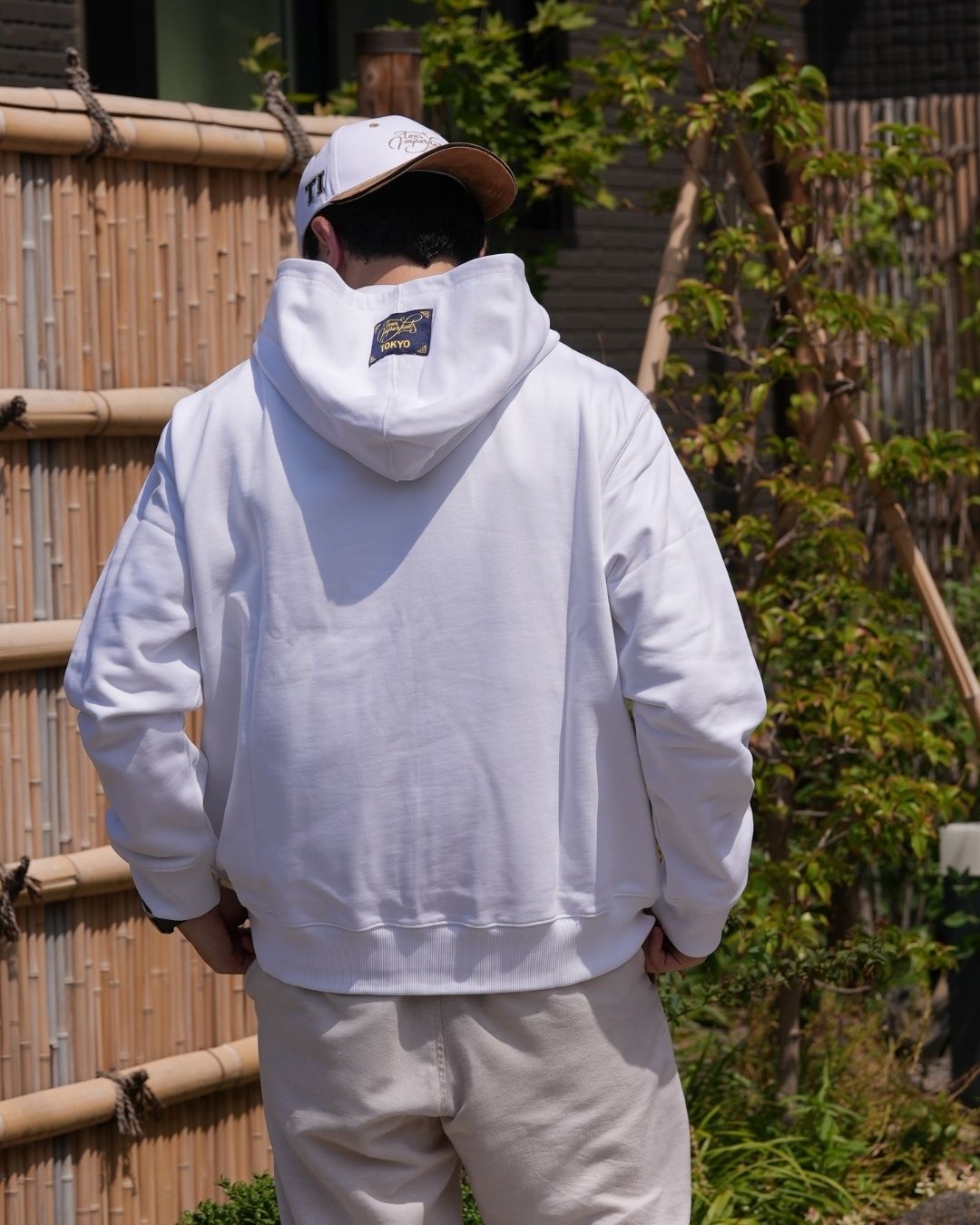 Le hoodie blanc Basics de Tous Imparfaits, porté par un modèle homme de dos en extérieur