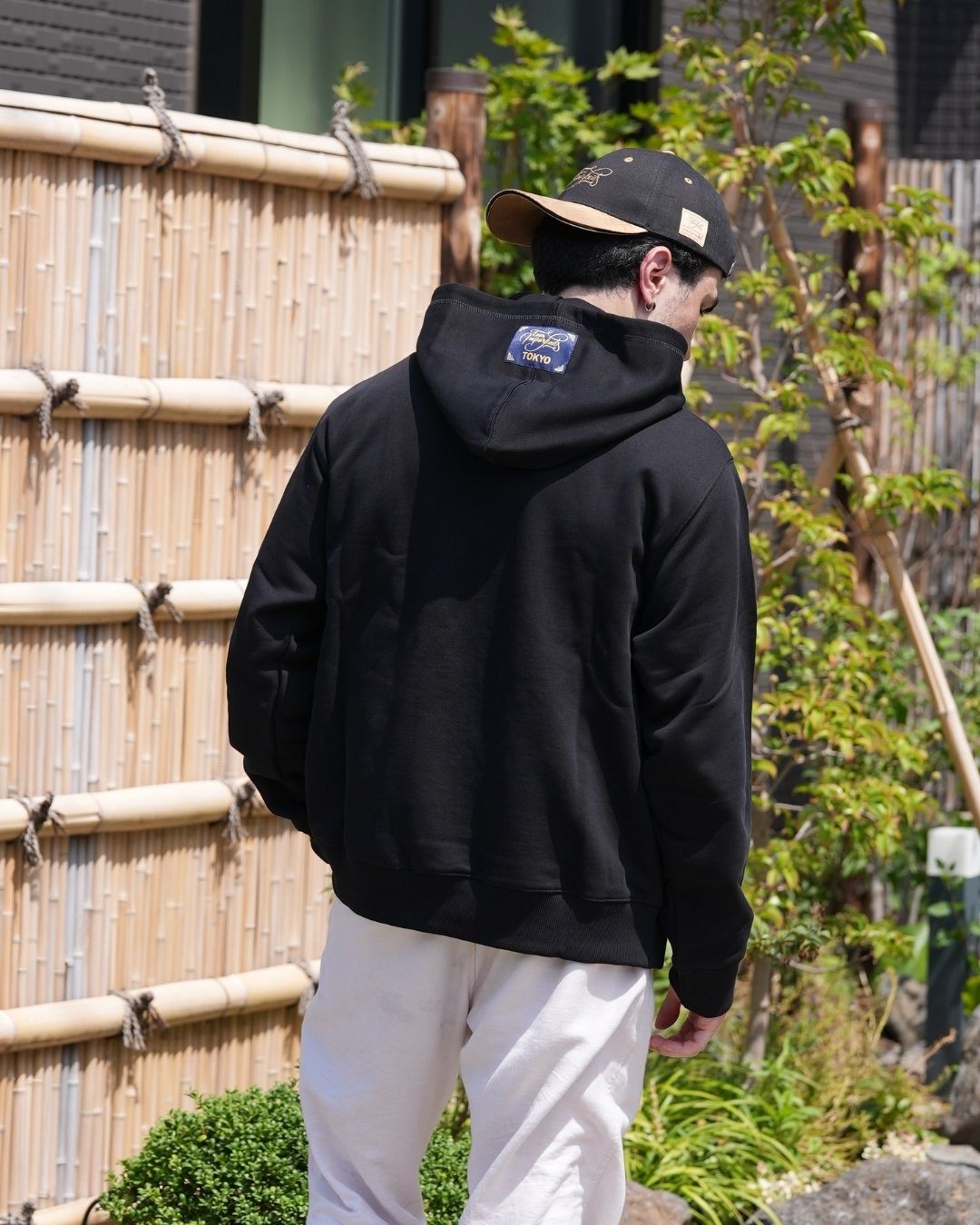 Léo de dos, portant le hoodie Basics noir de la marque Tous Imparfaits, en extérieur