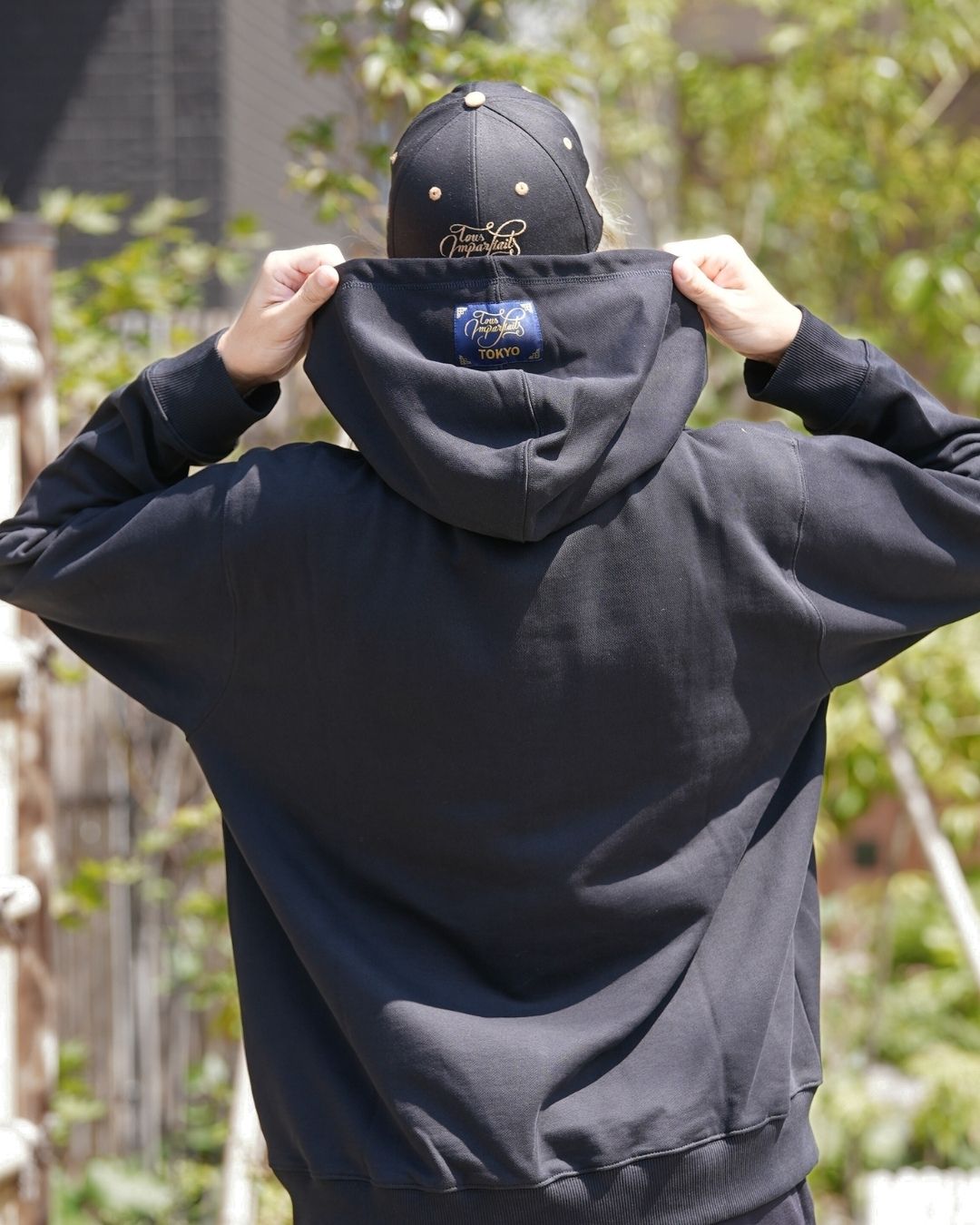Modèle homme portant le hoodie noir Basics de Tous Imparfaits, de dos en montrant la capuche