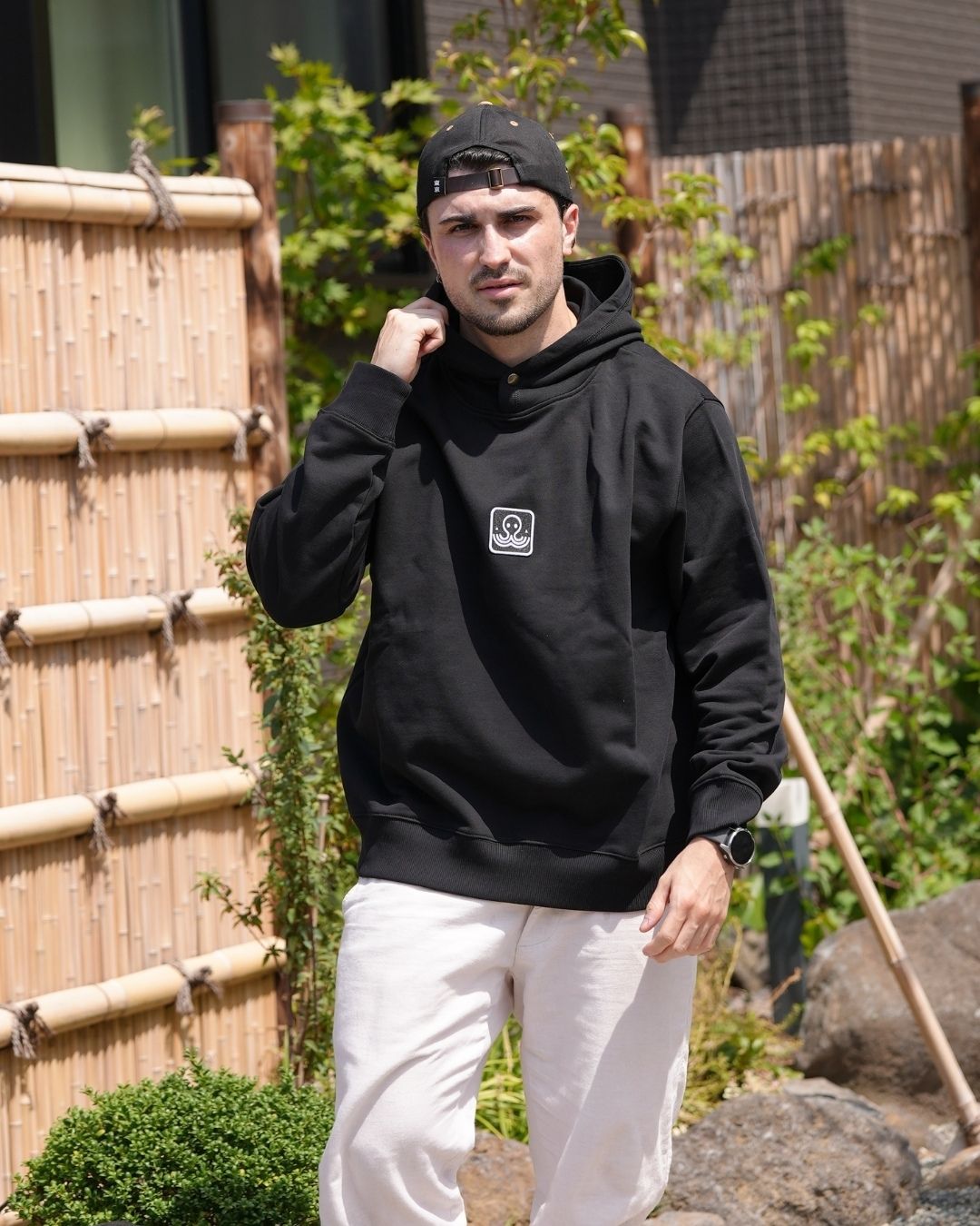 Léo d'Ici Japon Corp portant le hoodie Basics noir en extérieur, regardant la caméra