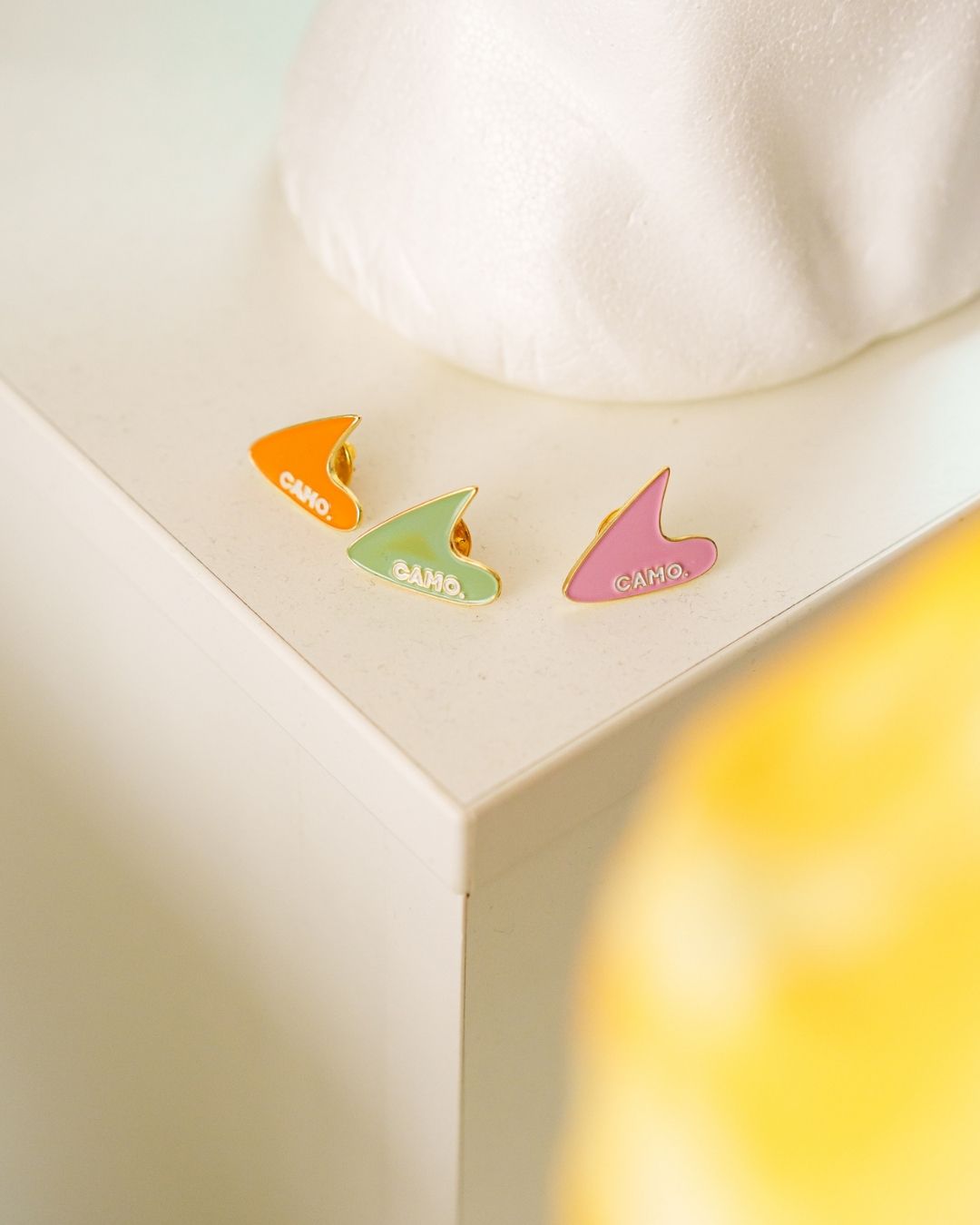 Les 3 pin's de la collection camo, orange, vert et rose, aligné sur une table